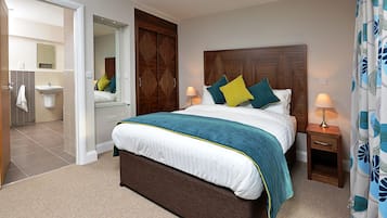 Un dormitorio con una cama grande, cabecera de madera, mesitas de noche, un espejo y un baño visible a través de una puerta abierta.