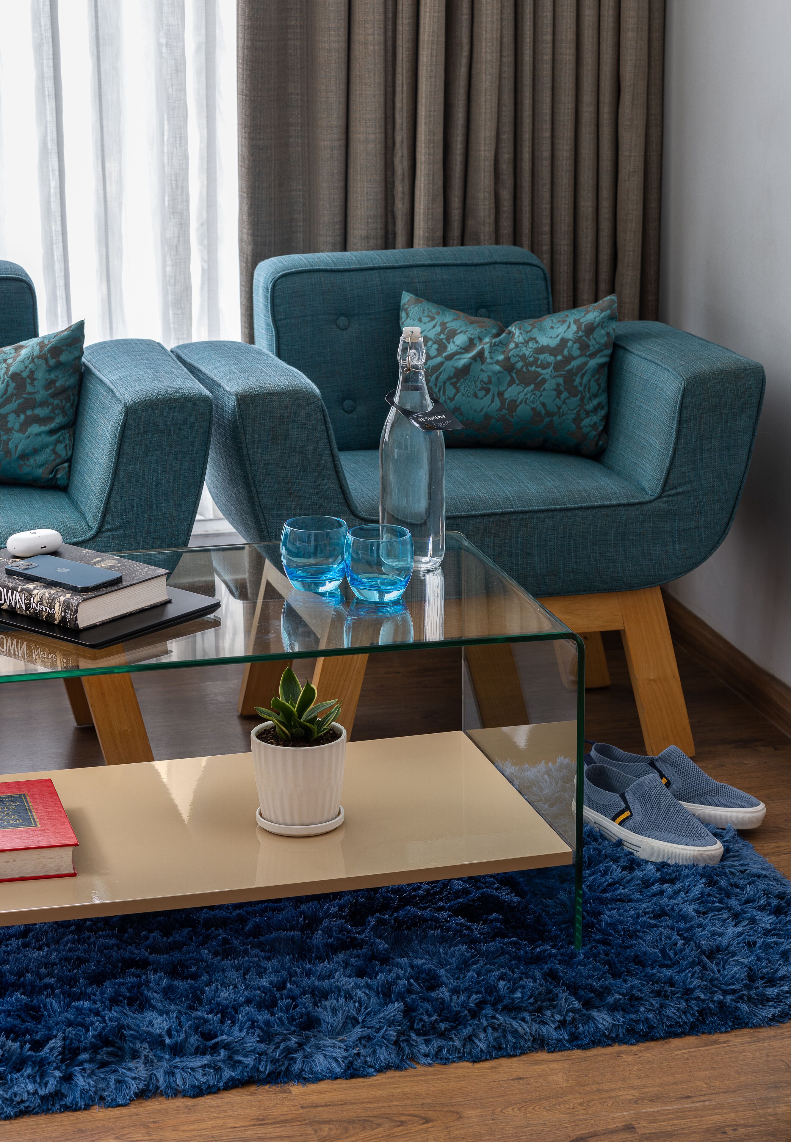 A modern living room with teal sofas, a glass coffee table, and a blue rug.