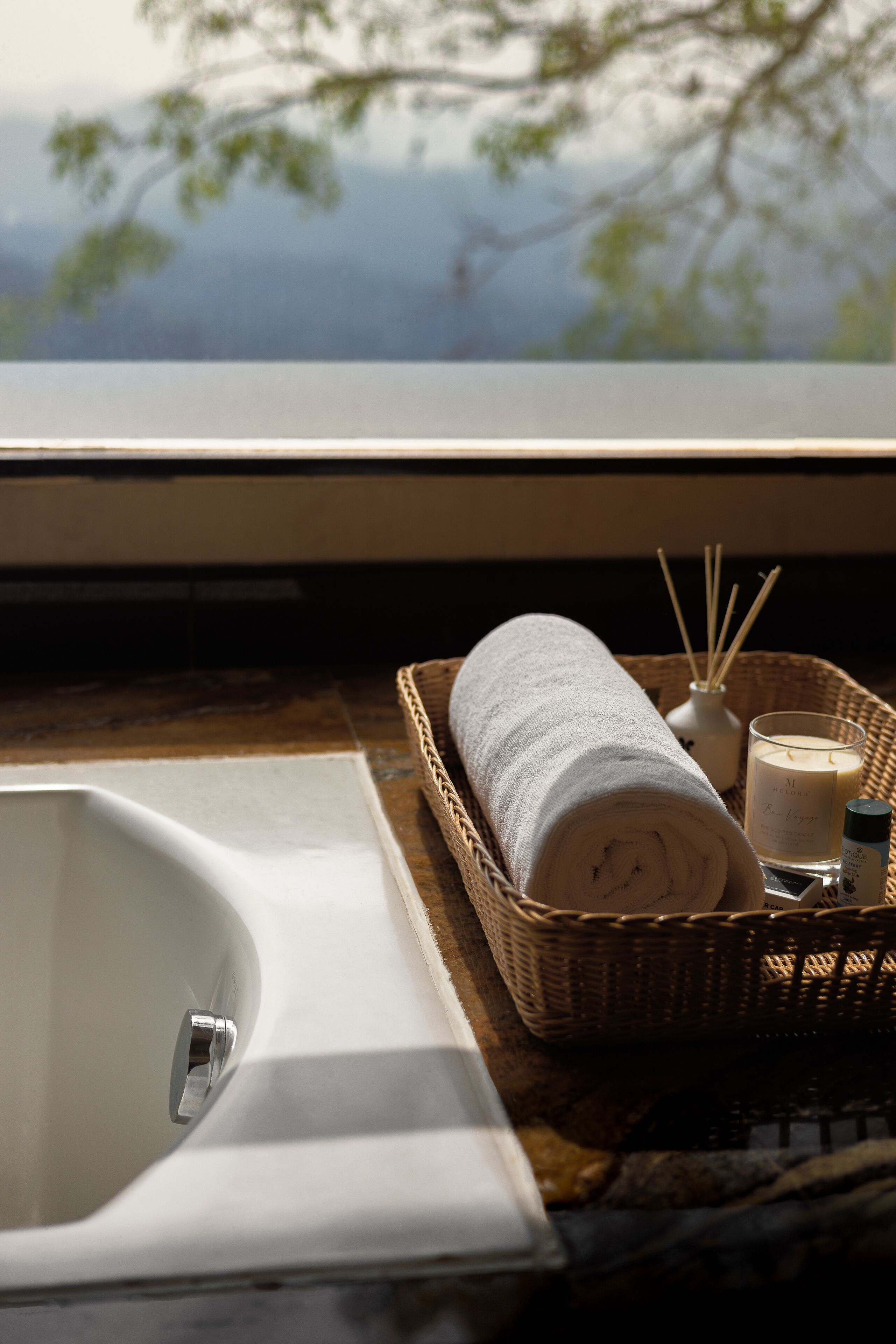 A bathroom with a white bathtub, a wicker basket with a rolled towel, a candle, and reed diffusers.