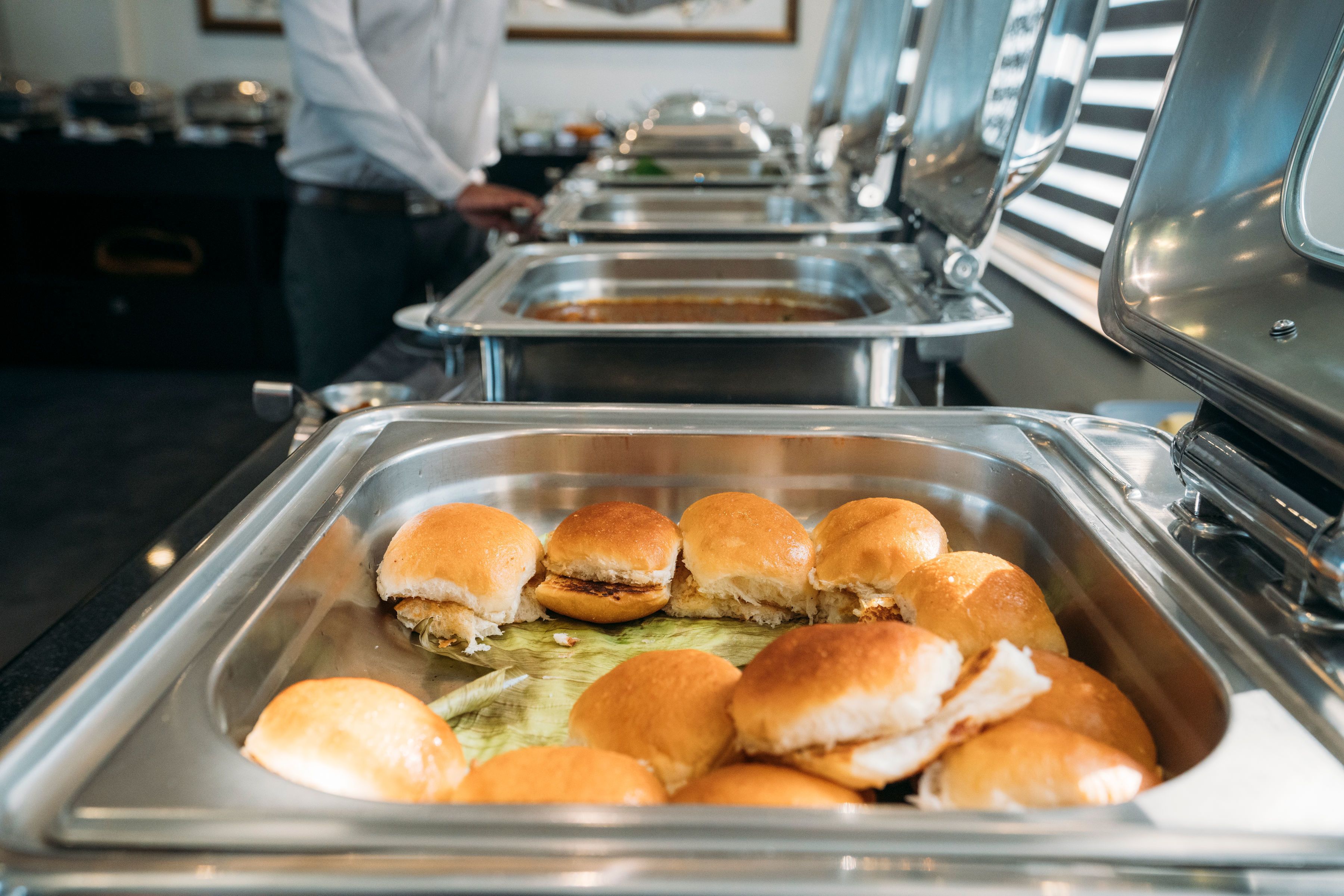 A buffet with various food items, including sandwiches and rolls, arranged in metal trays.
