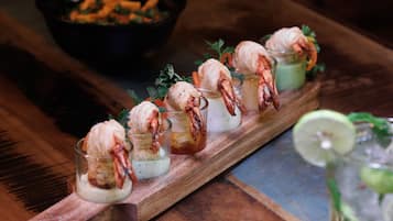A wooden table with a glass tray holding shrimp appetizers and a bowl of vegetables in the background.