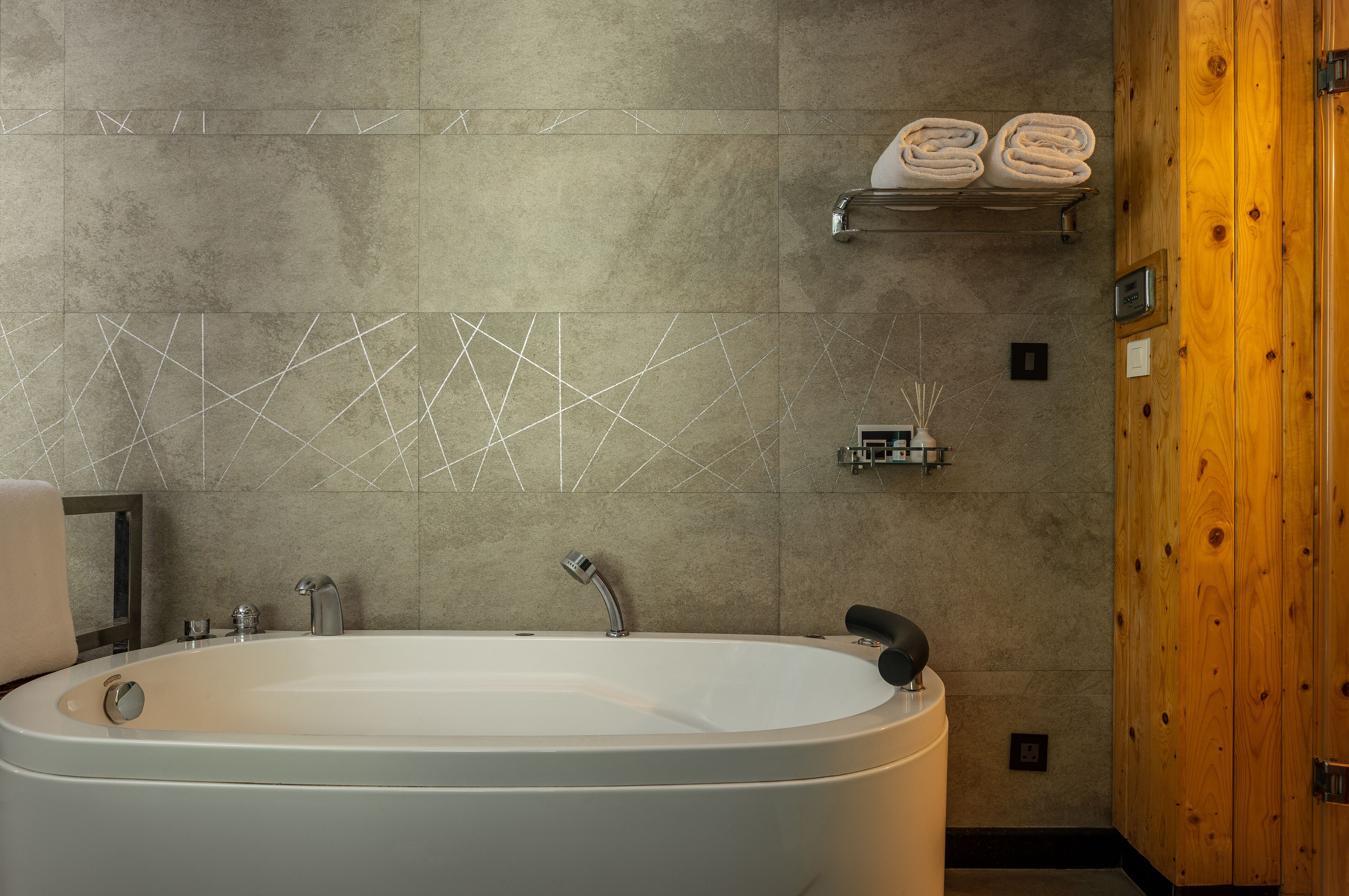 Un baño moderno con una bañera independiente, un perchero con toallas dobladas y una pared decorativa con diseños geométricos.