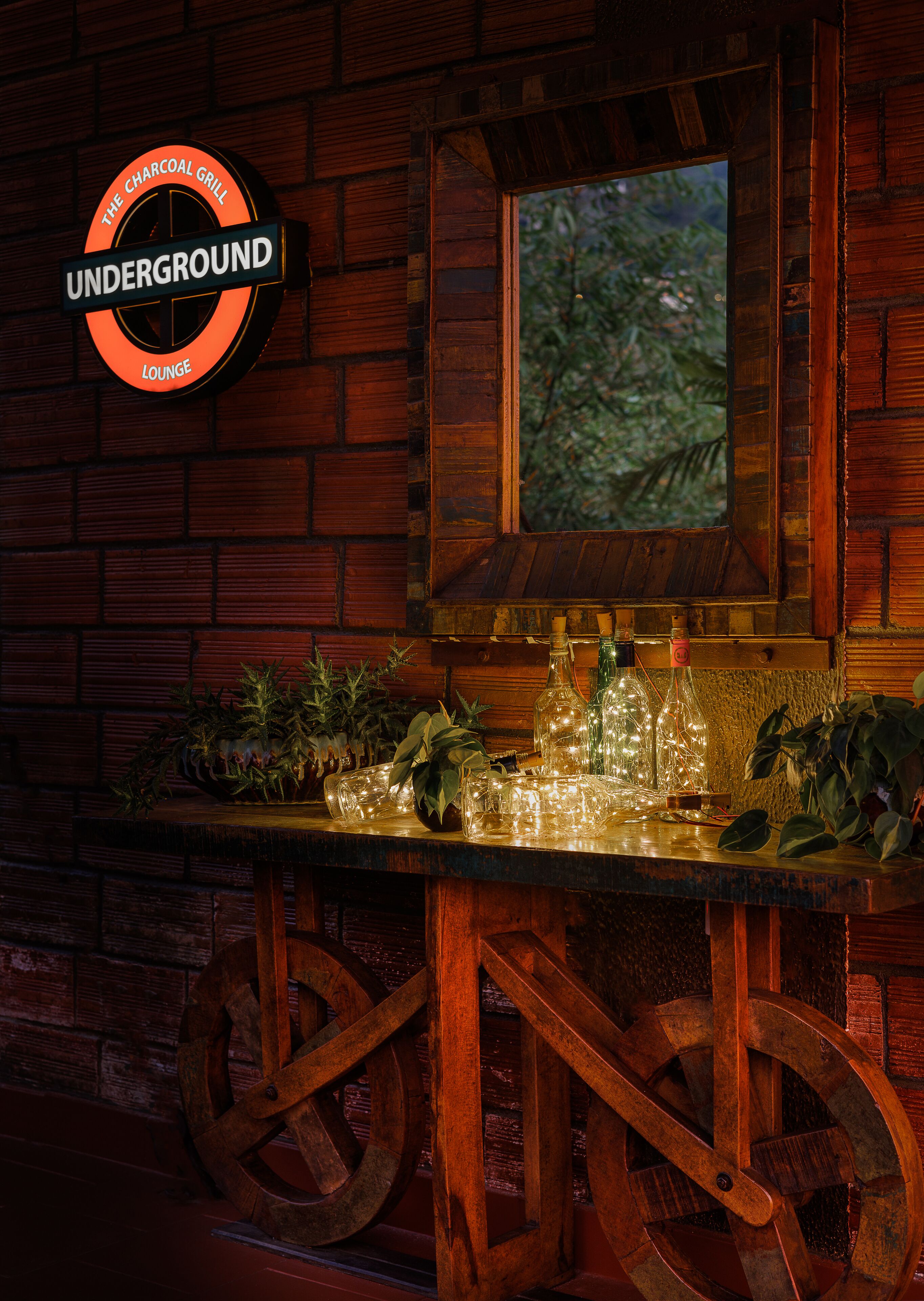 A bar area with a sign reading "The Charcoal Grill Underground Lounge," wooden barrel stools, and a window overlooking greenery.