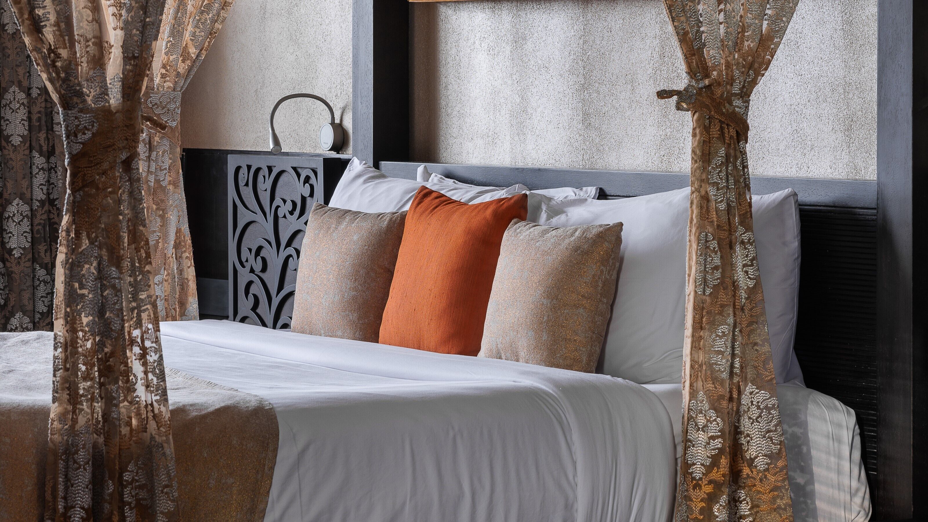 A bed with white bedding, a headboard with a decorative panel, and a pair of curtains.