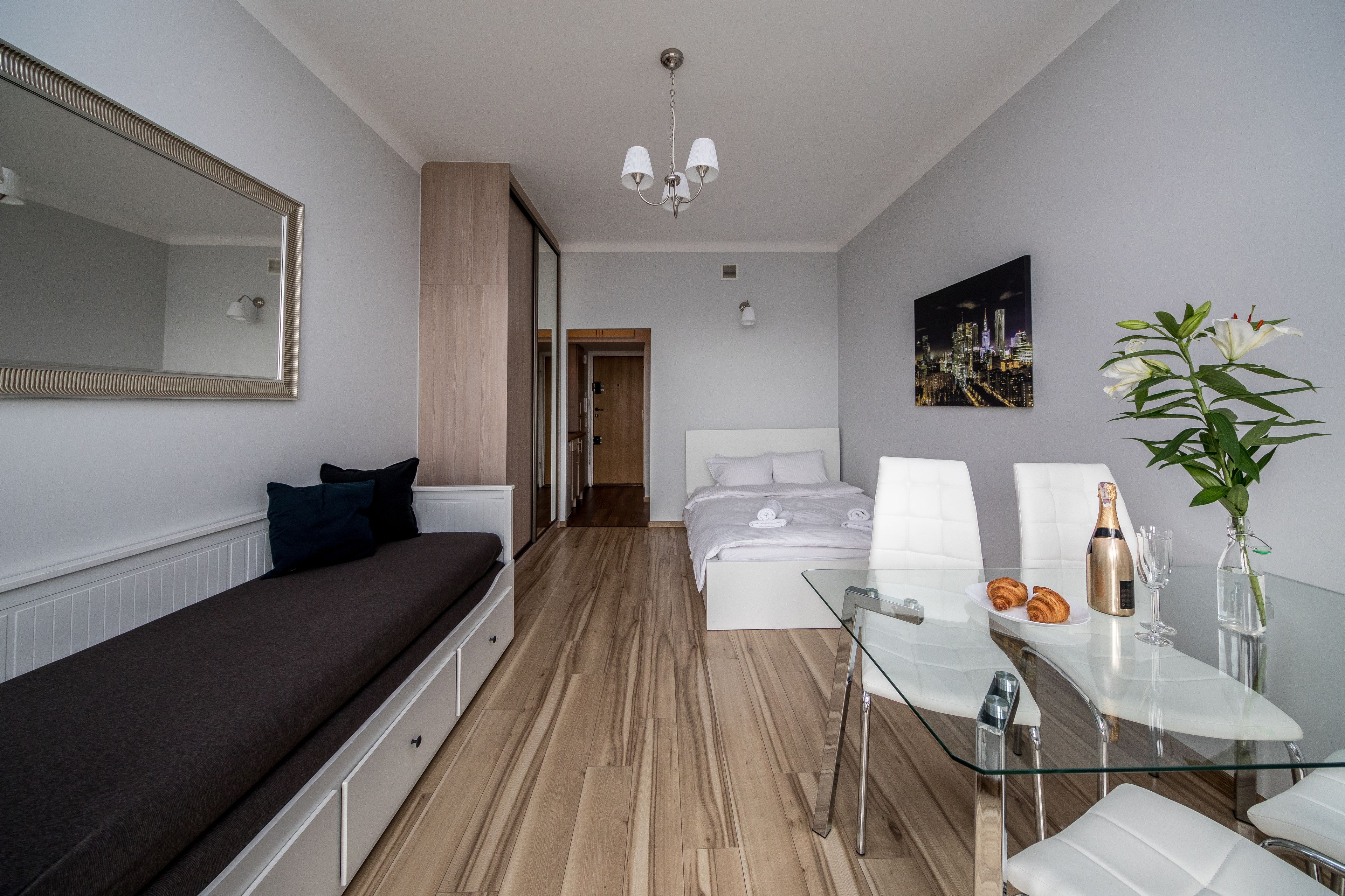 Ein modernes Schlafzimmer mit einem Bett, einer Couch, einem Glastisch und einem großen Spiegel.