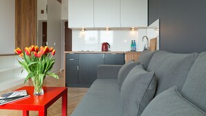A modern kitchen with white cabinets, a red kettle, and a grey sofa in a living area. - Smolna Apartments by Your Freedom (Warsaw)