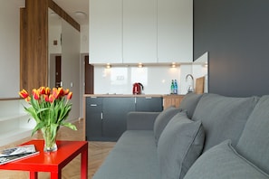 Une cuisine moderne avec des meubles blancs, une bouilloire rouge et un canapé gris dans l’espace salon.