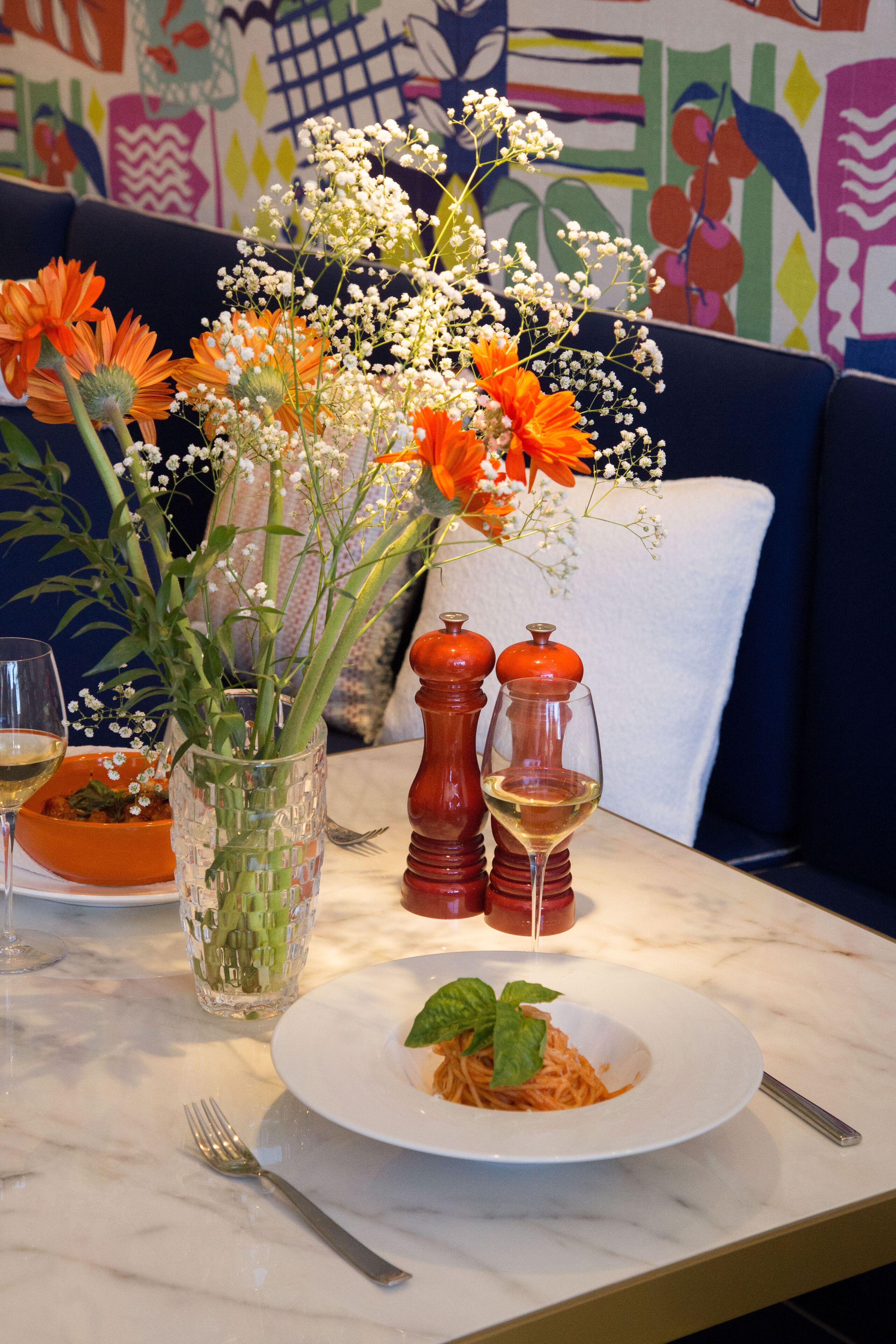 Et spisebord med en tallerken pasta, en vase med blomster og to salt- og peberkværke.