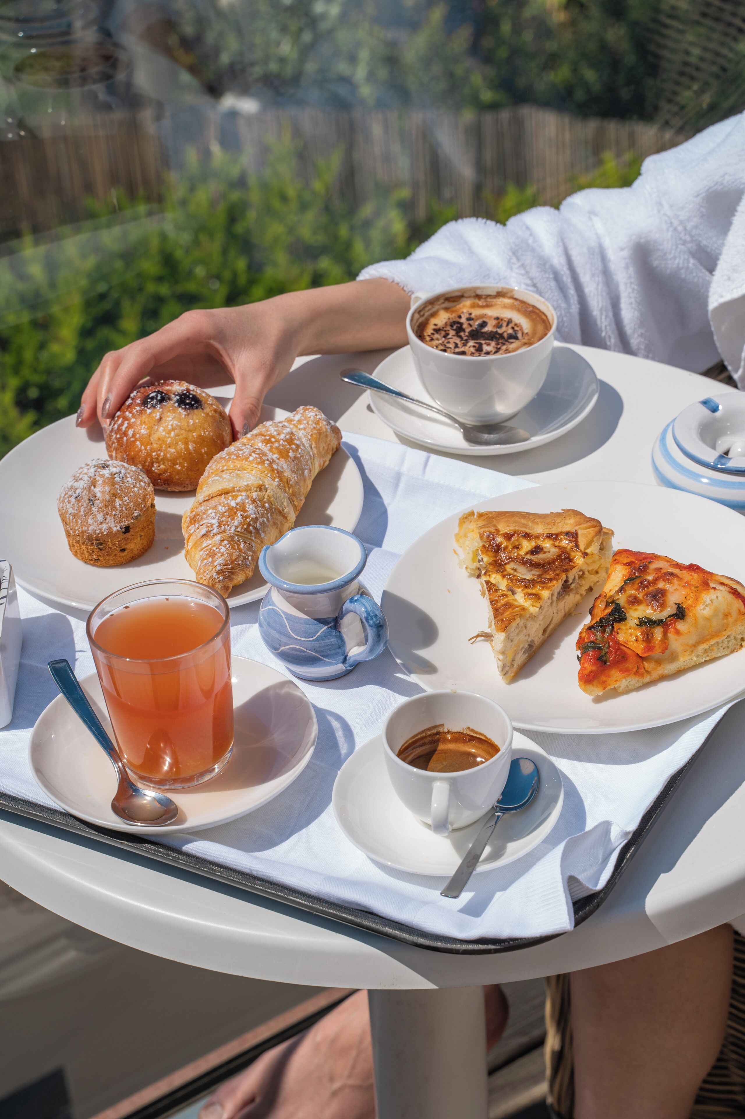 Una mesa con pasteles, una porción de pizza, una taza de café y un vaso de té.
