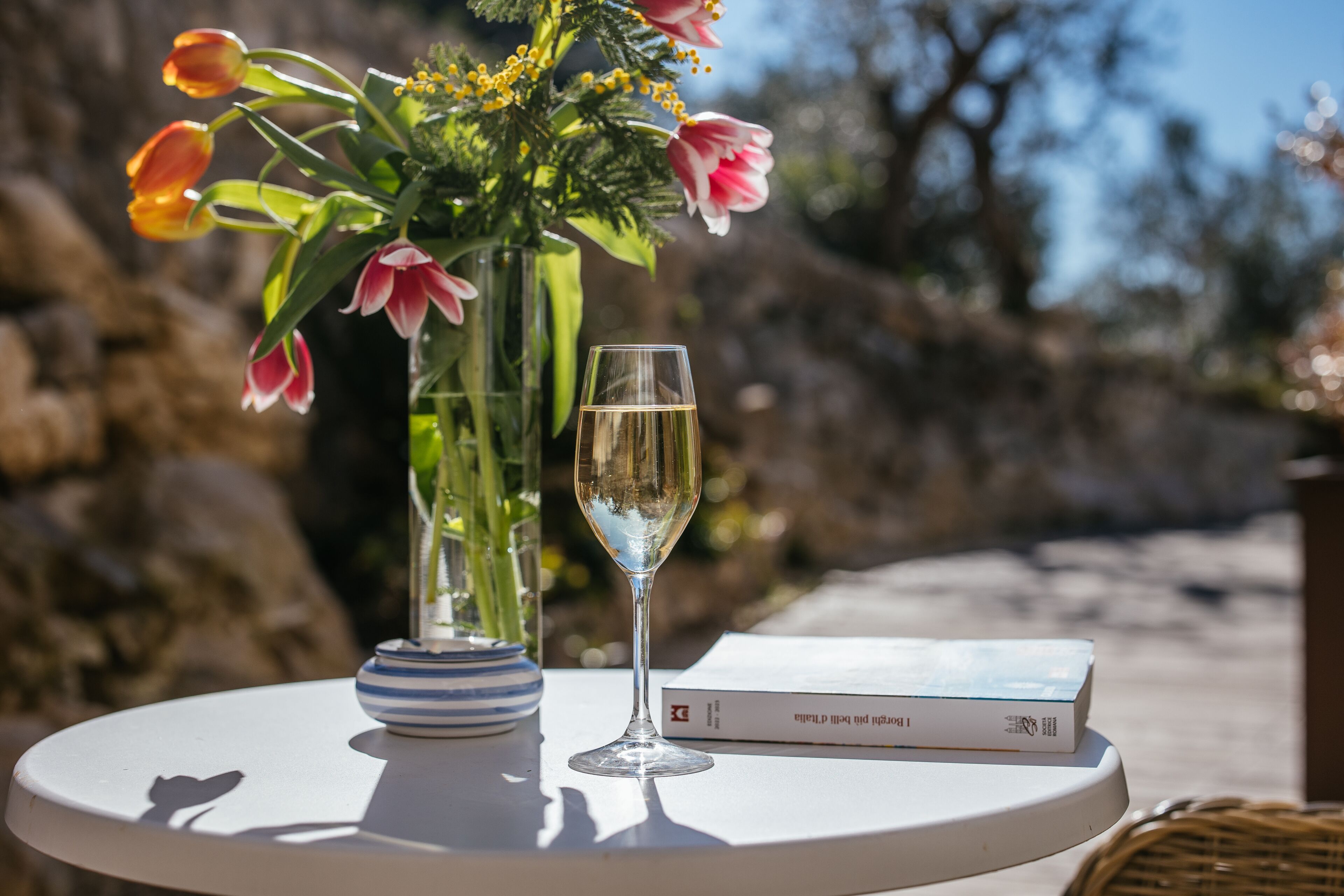 Une table avec un verre de vin, un livre et un vase de fleurs.