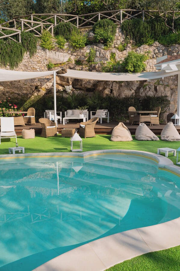 Un área de piscina con sillones, una pequeña mesa y un muro de piedra de fondo.