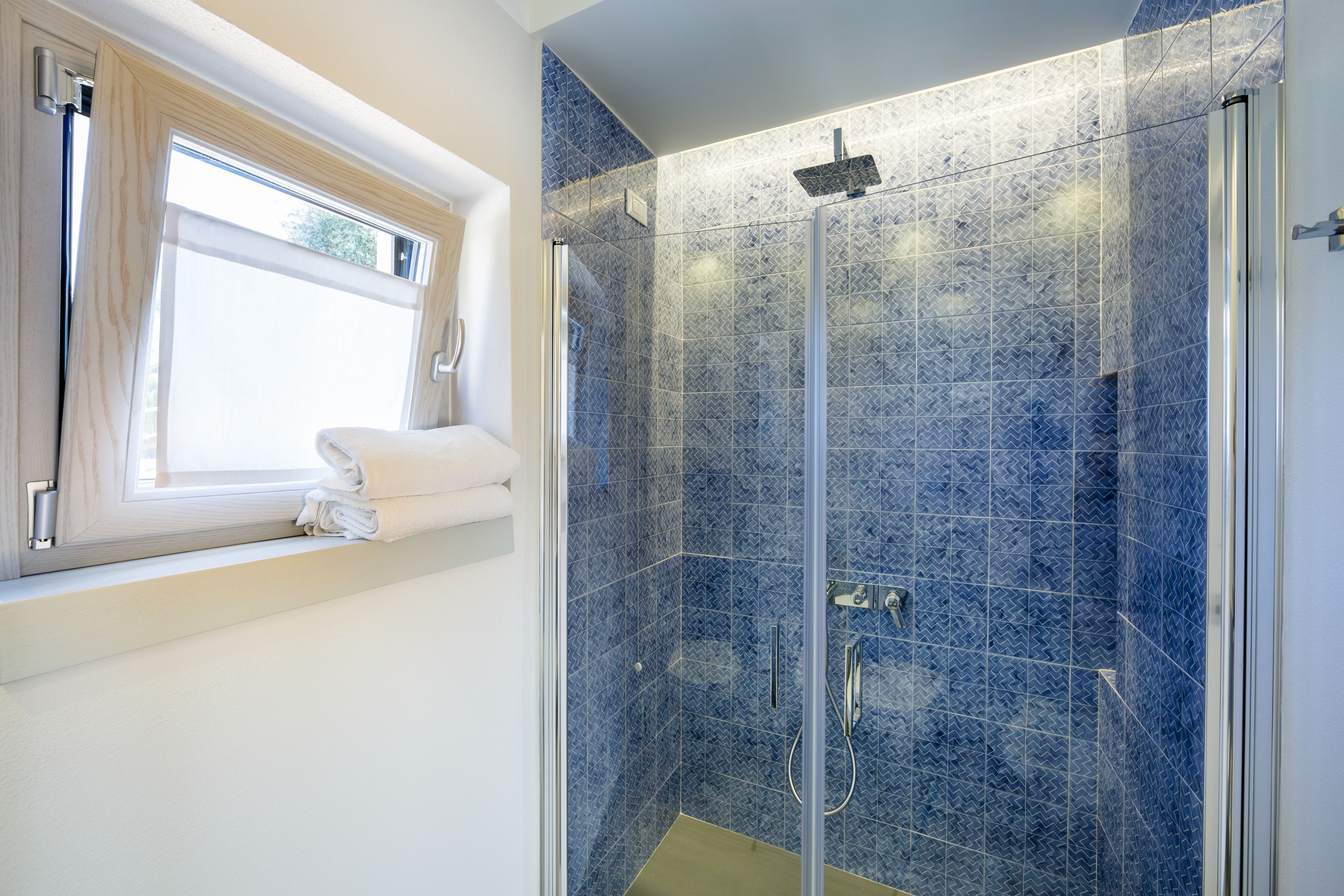 Ein modernes Badezimmer mit einer gläsernen Duschkabine, einem Fenster mit Handtuchhalter und einer Wand mit Musterfliesen.