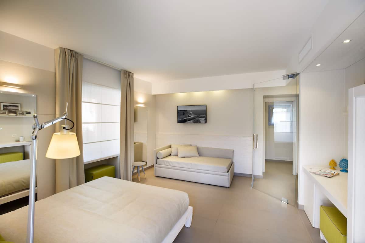 A modern hotel room with a bed, a sofa, a desk, and a chair.