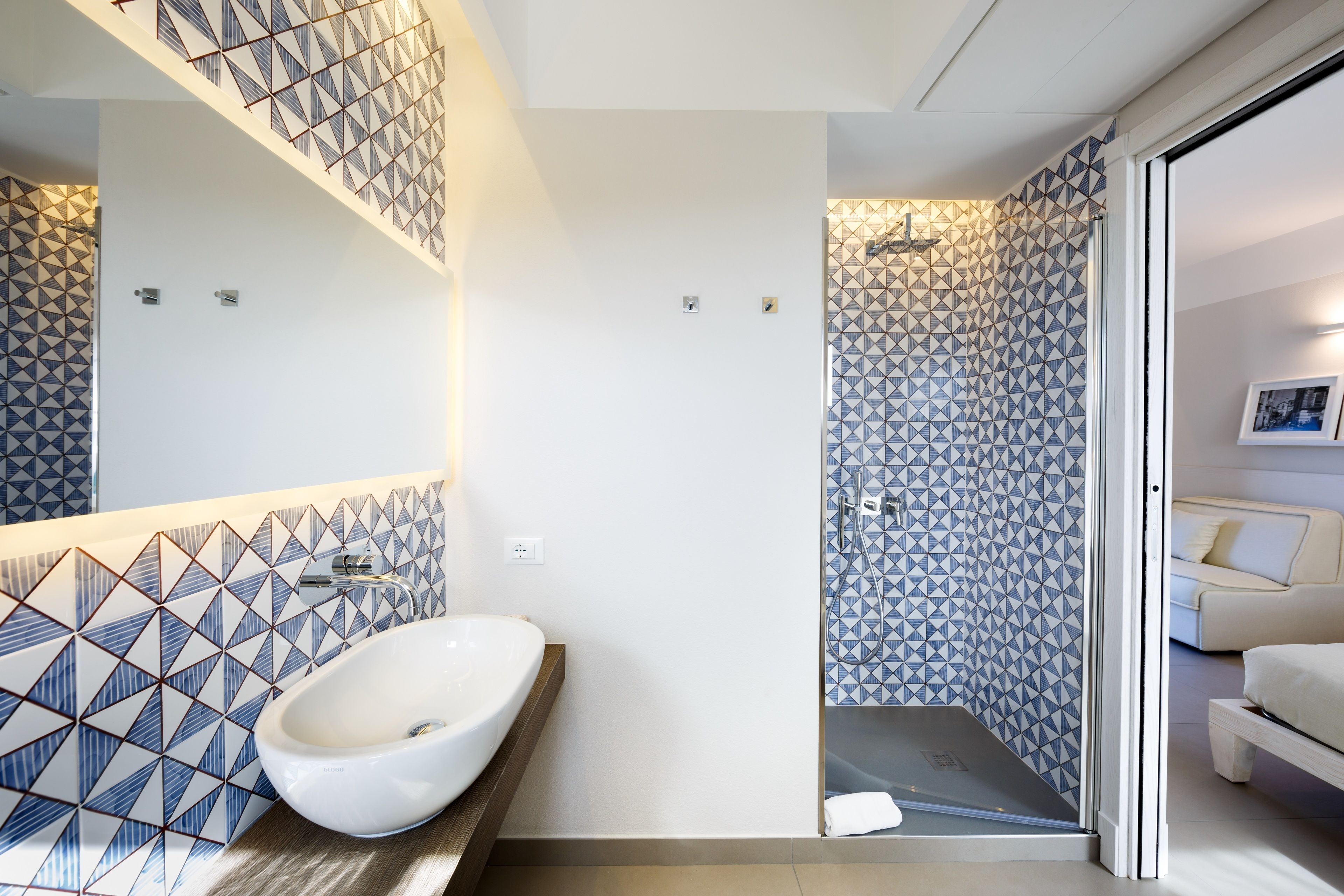 A modern bathroom with a geometric tile backsplash, a white sink, and a shower area.