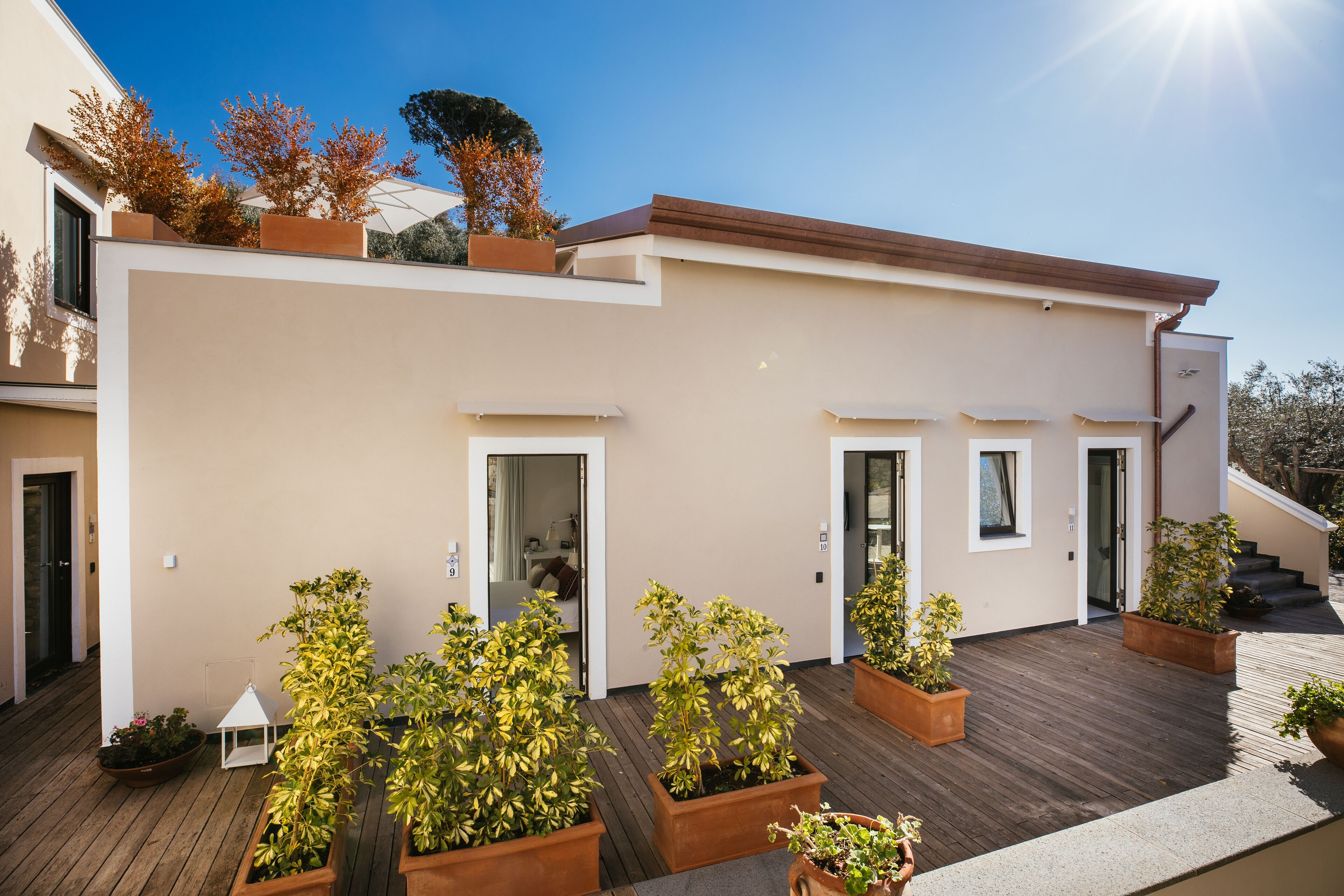 A modern residential building with a flat roof, multiple entry doors, and a wooden deck with potted plants.