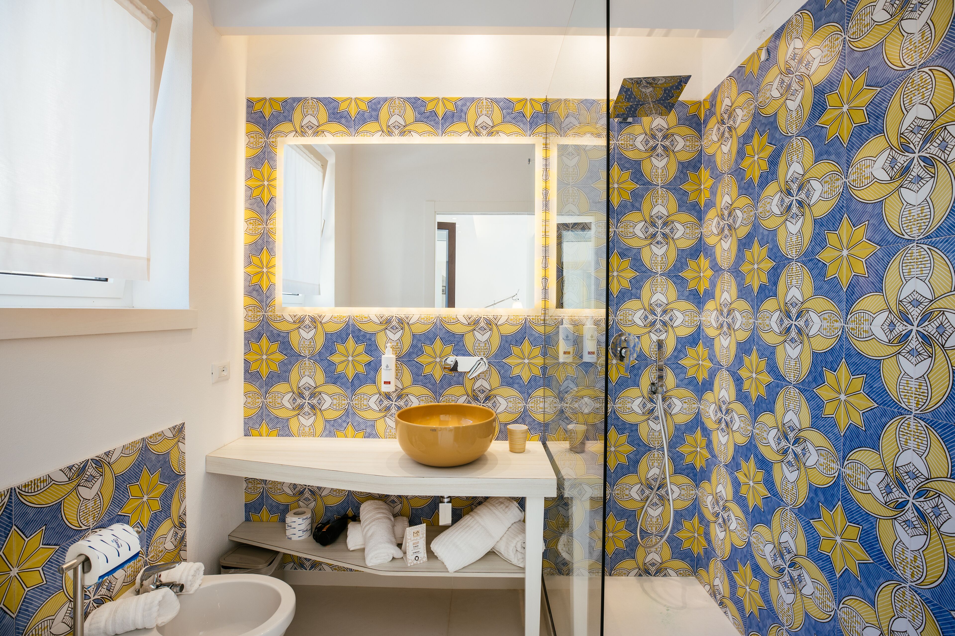 Un baño con un espejo grande, un lavabo y baldosas con diseño.