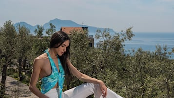Uma pessoa sentada numa varanda com vista para a paisagem costeira e montanhas ao longe.