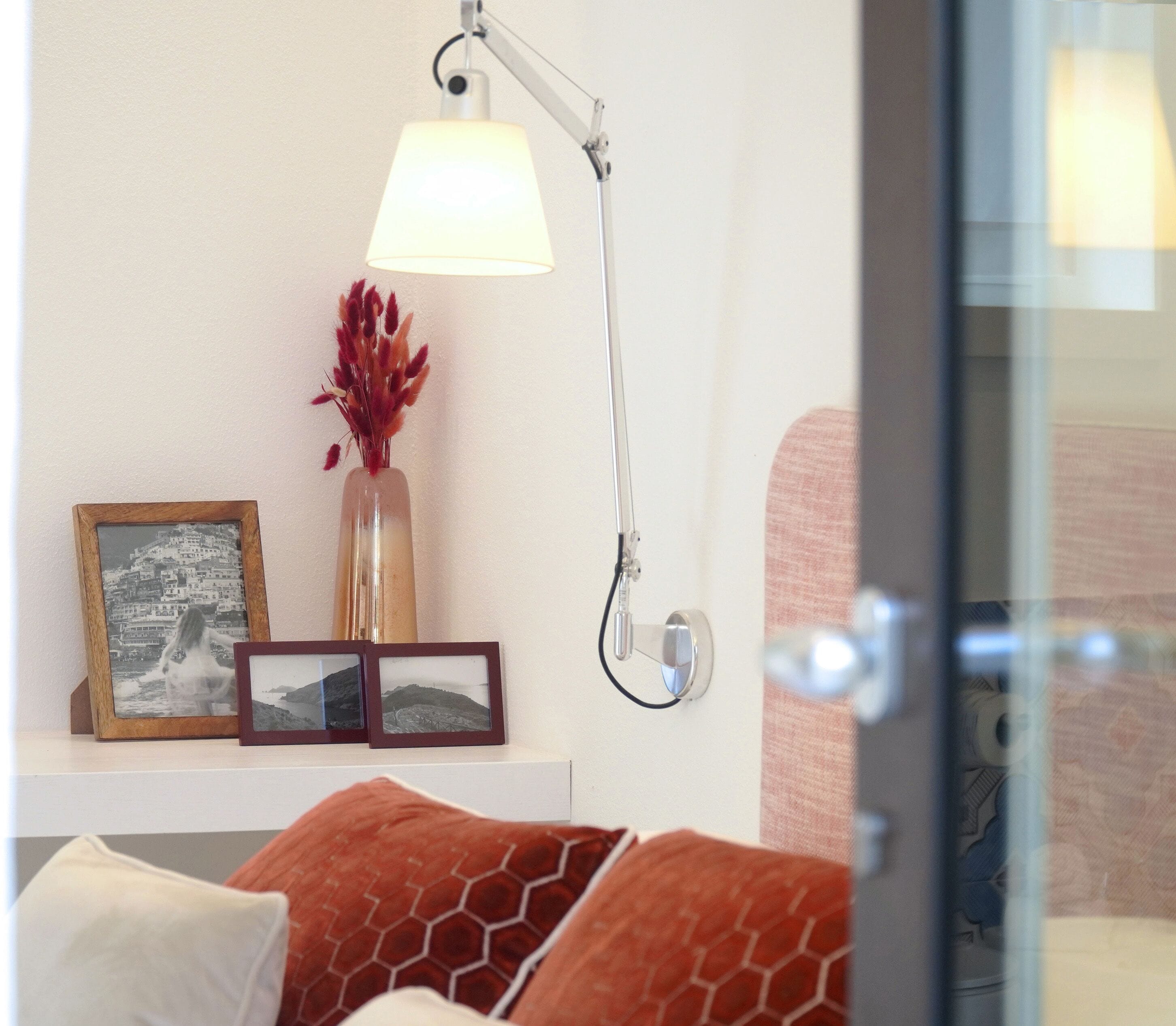 A bedroom with a bed, a bedside table with a lamp, a vase with red flowers, and framed pictures.
