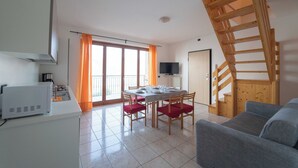Una sala de estar moderna con un sofá gris, una escalera de madera, un comedor con mesa y sillas, y una zona de cocina con microondas.