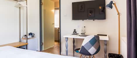A hotel room with a bed, a desk with a chair, a television, and a waste bin.
