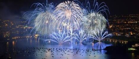 A nighttime view of a fireworks display over a body of water with boats, reflecting the lights.