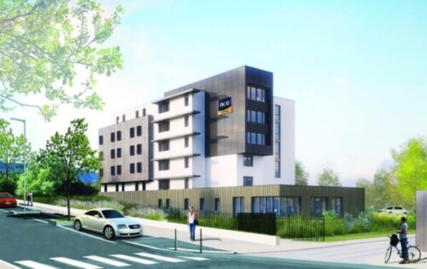 Un edificio moderno de varios pisos con techo plano y un llamativo letrero 'ACE' en la fachada, con un paso de peatones enfrente.