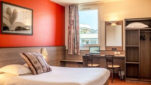 Habitación de hotel con cama, escritorio, computadora, silla, armario y ventana con vista a edificios.