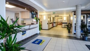 Zona de recepción de un hotel con mostrador, un letrero que muestra el nombre del hotel y un pasillo que conduce a otras habitaciones.