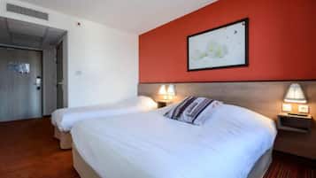 A hotel room with two beds, a red accent wall, and a framed picture above the beds.