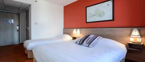 A hotel room with two beds, a red accent wall, and a framed picture above the beds.