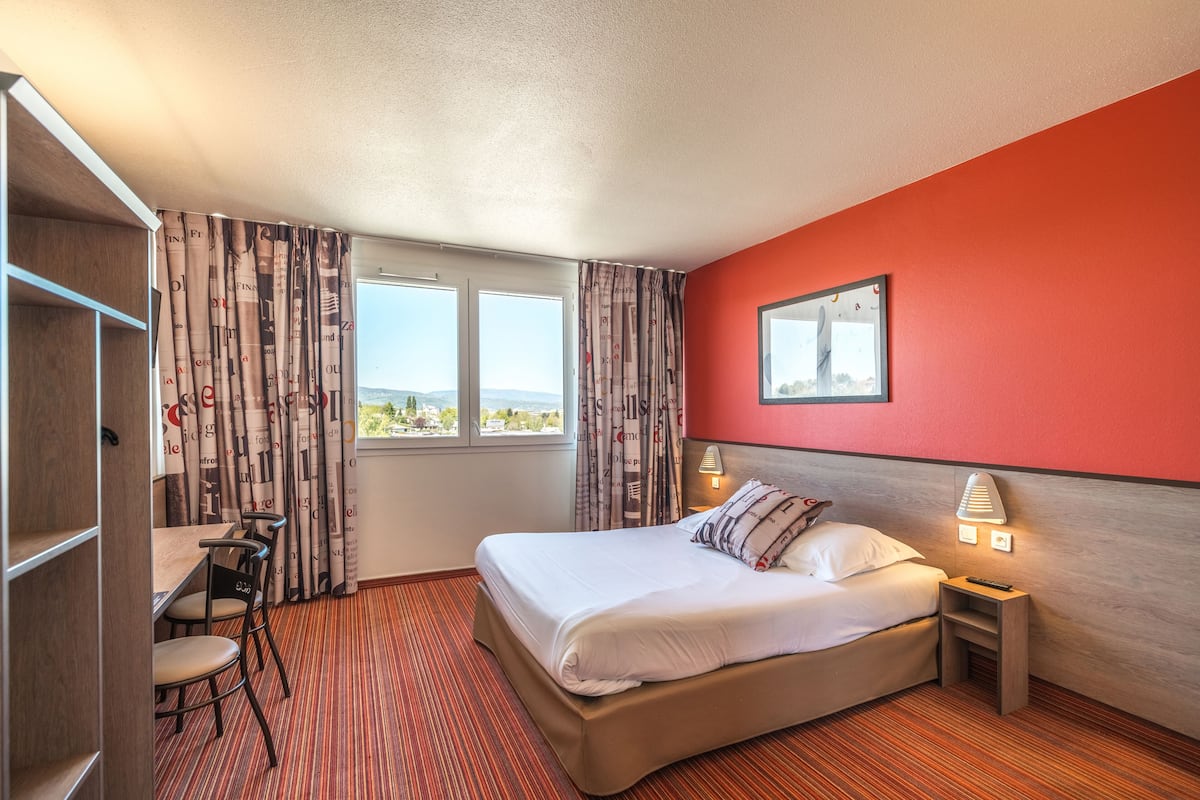 A hotel room with a bed, a desk, and a view of the outdoors.