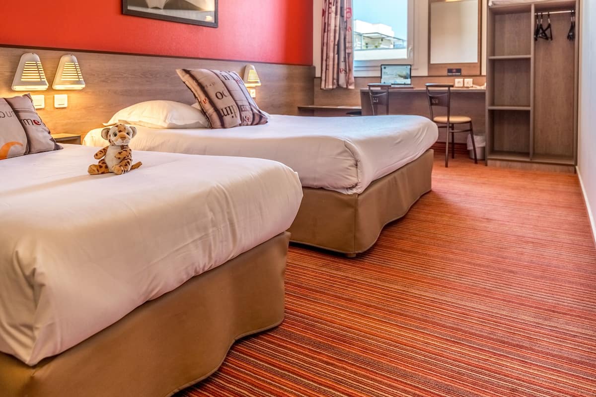 A hotel room with two beds, a desk, a chair, a wardrobe, and a window with curtains.