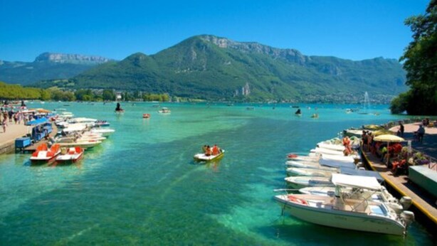 Un puerto deportivo con barcos amarrados, un mar azul cristalino y montañas al fondo.