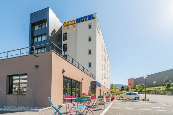 ACC Hotel features a modern exterior with a flat roof and balcony, surrounded by lush greenery and a parking area.
