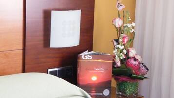 Une chambre d’hôtel avec une tête de lit en bois, une table de chevet sur laquelle se trouve un livre, un vase avec des fleurs et un rideau.