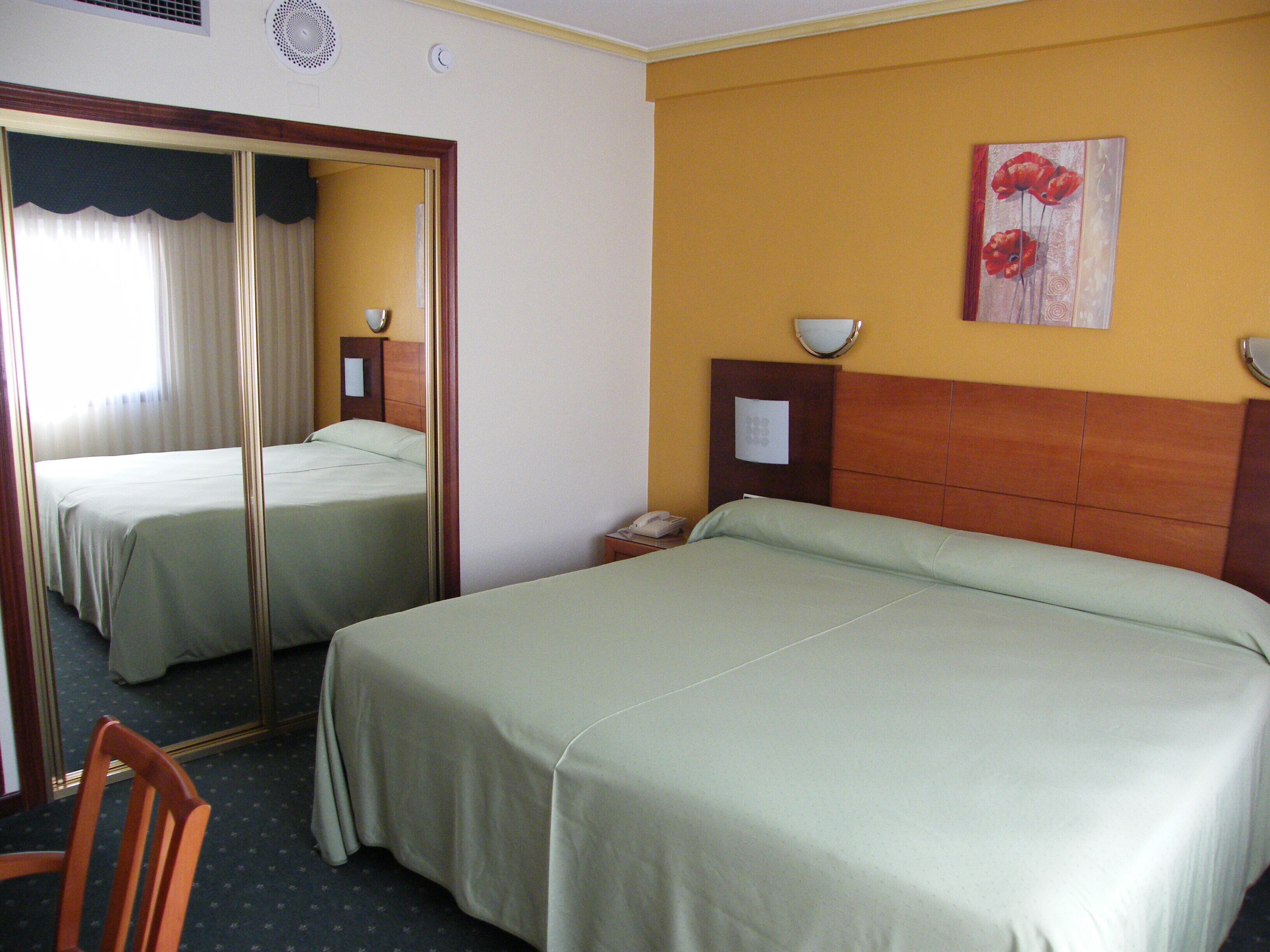 A hotel room with two beds, a mirror, a painting, and a telephone.