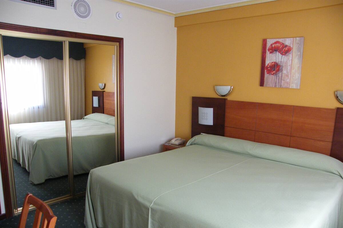 Ein Hotelzimmer mit zwei Betten, einem Spiegel, einem Nachttisch mit Lampe und einem Bild an der Wand.