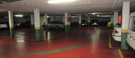 A multi-level parking garage with concrete pillars, red flooring, and several parked cars.