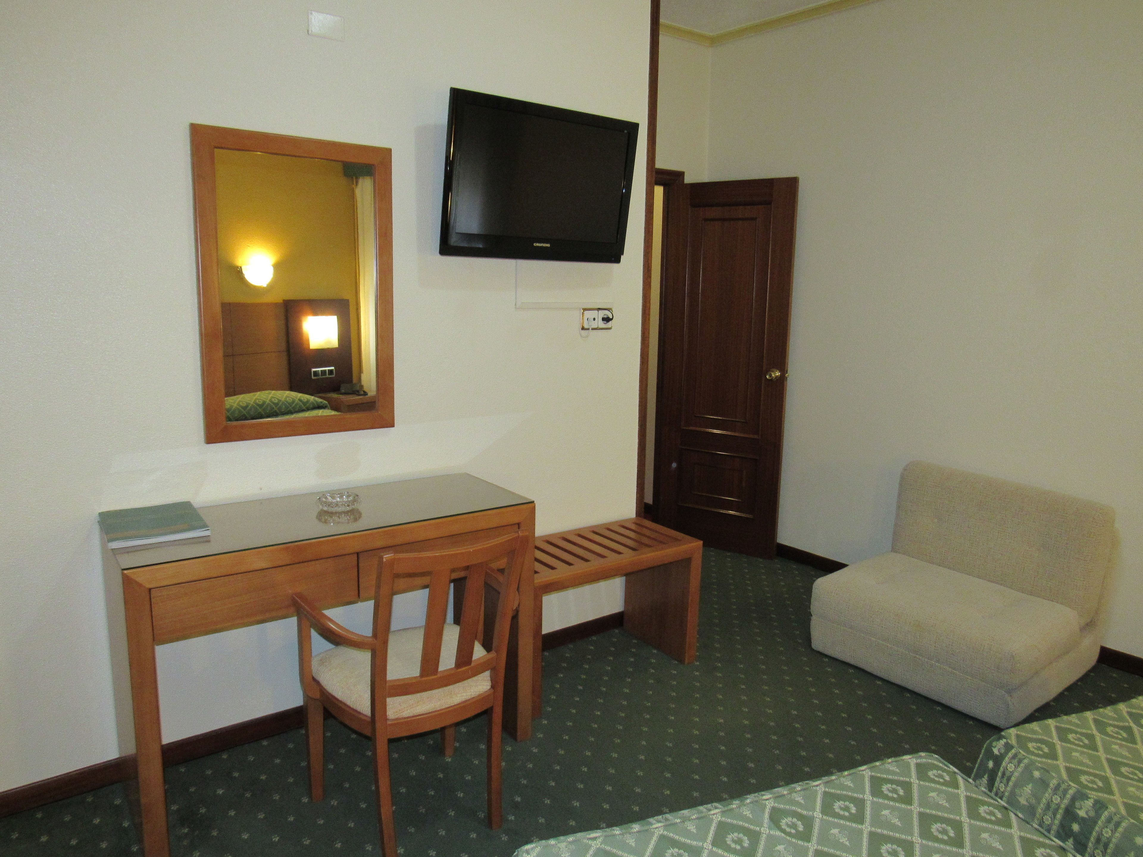 Habitación de hotel con un escritorio de madera, una silla, un televisor, una puerta y un sofá.
