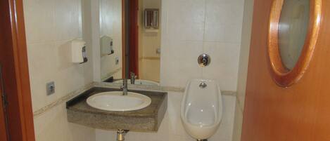 Un baño con lavabo, espejo, orinal y puerta de madera.