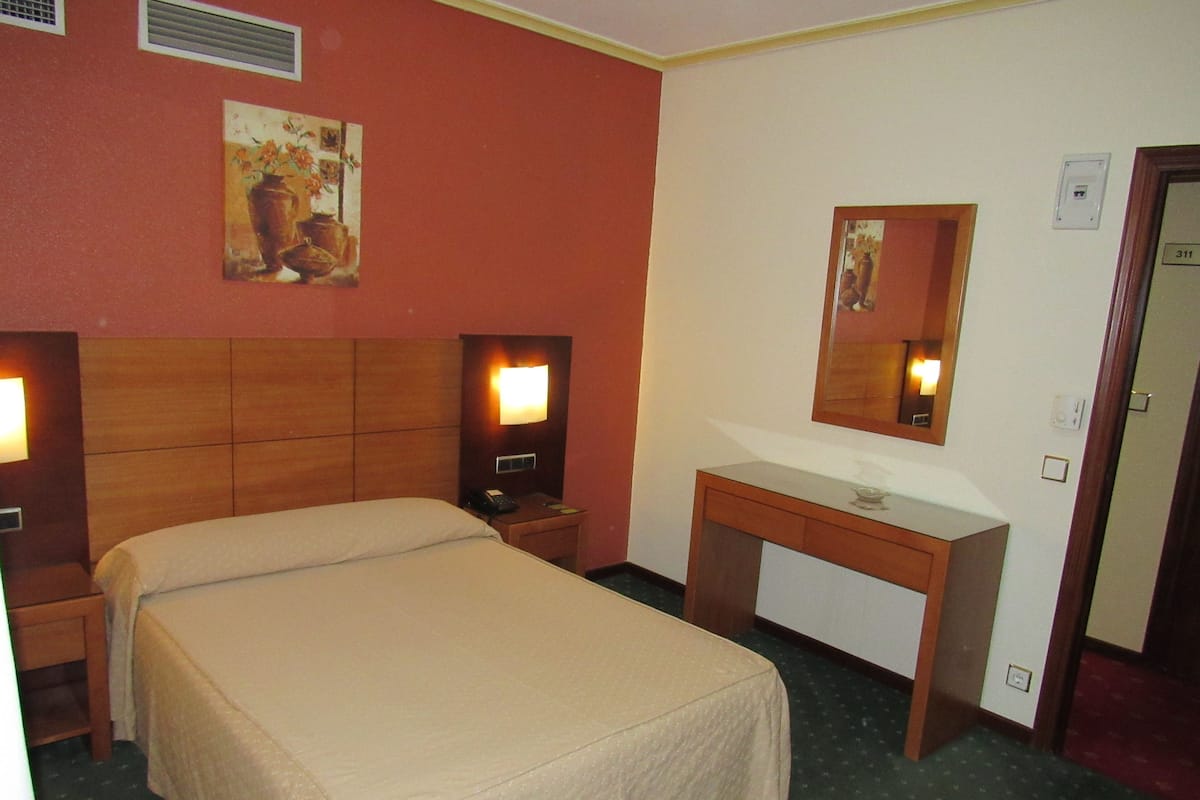 Ein Hotelzimmer mit einem Bett, Nachttischen, einem Spiegel und einem kleinen Schreibtisch.