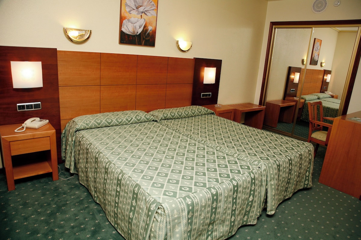 Habitación de hotel con una cama grande, mesitas de noche, un espejo y un teléfono.