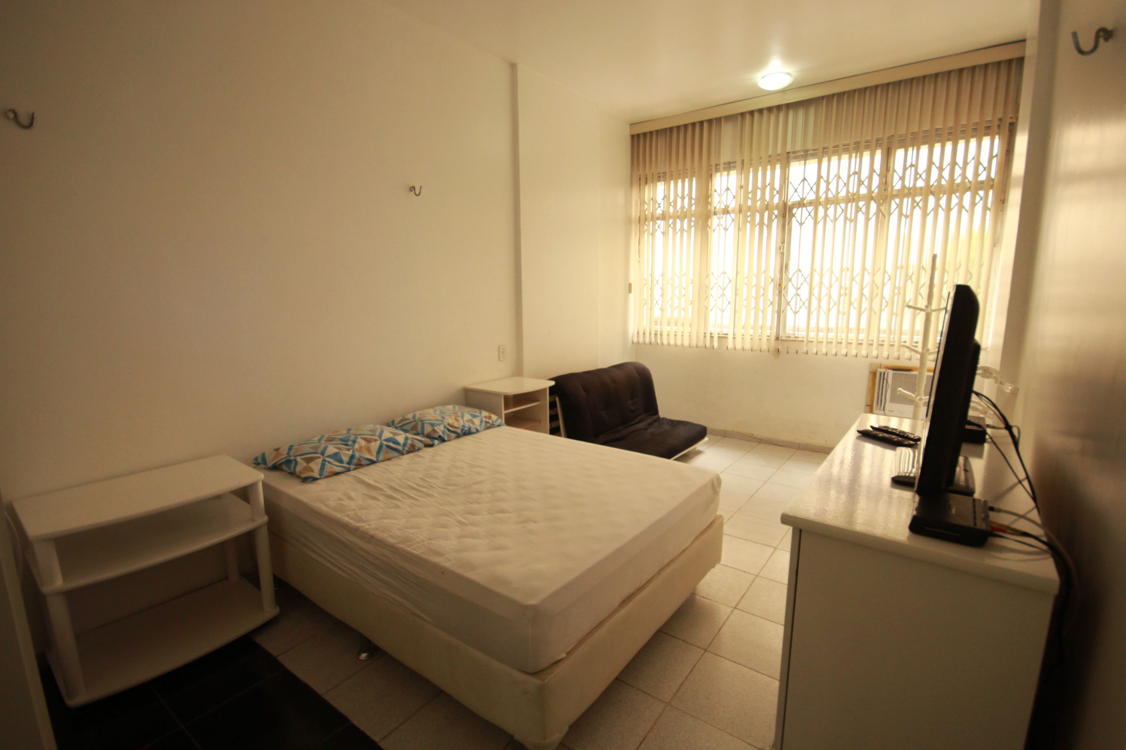 A small, clean room with a bed, a desk, a chair, and a TV.