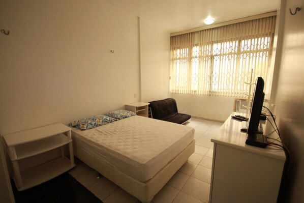 A small, clean room with a bed, a desk, a chair, and a TV.