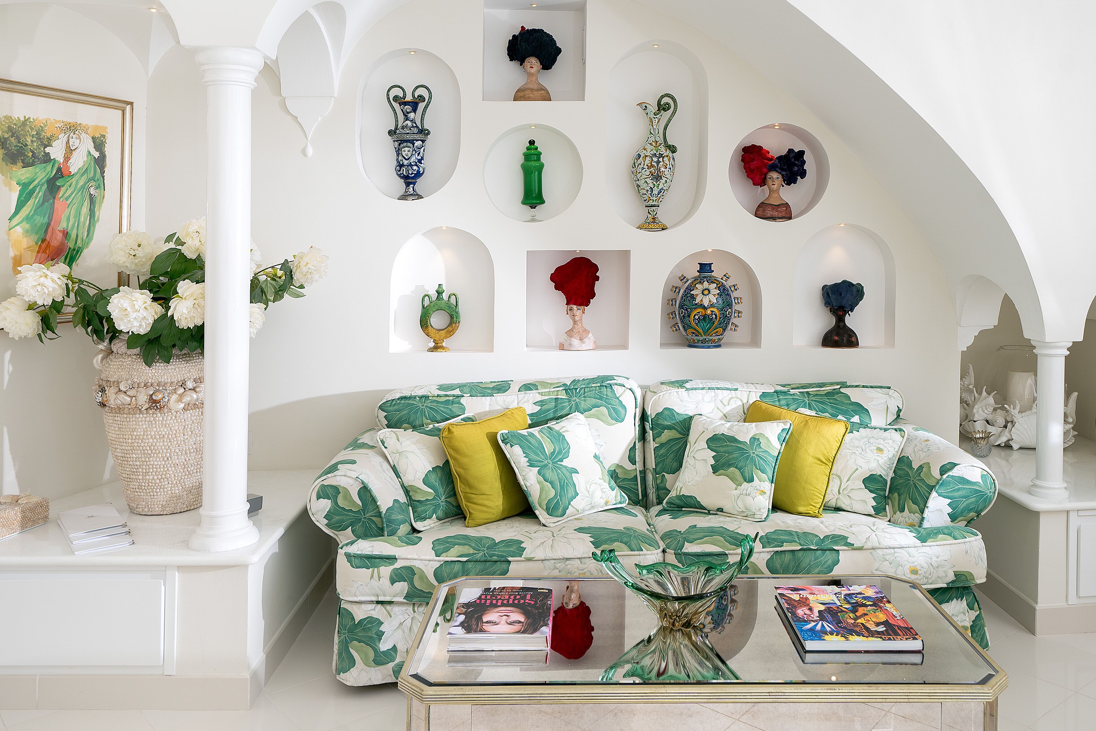A living room with a floral sofa, a coffee table with books, and decorative items on the walls.