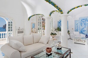 A spacious living room with a white sofa, a glass coffee table, and a view of the sea. - Villa Boheme Exclusive Luxury Suites (Positano)