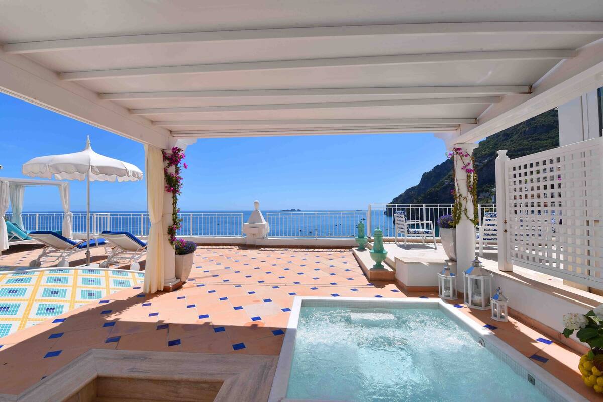 Un espace piscine sur le toit, offrant une vue sur la mer, avec des chaises longues et un jacuzzi.
