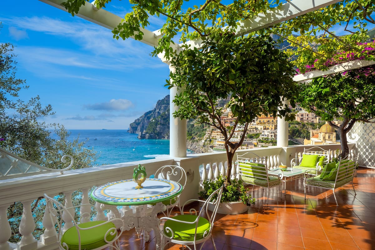 Une terrasse avec une table et des chaises, offrant une vue sur la côte, avec des bâtiments et des falaises.