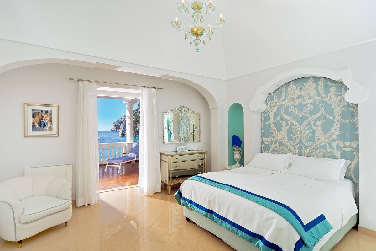 Une chambre avec un lit, une commode, une chaise et une vue sur la mer.