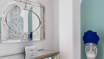 Ein Zimmer mit einer Spiegelwand, einem weißen Schminktisch mit Schubladen, einem kleinen Regal mit Dekoration und einer blauen Akzentwand.